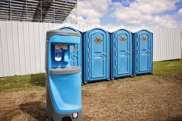 Portable hand-wash station standing beside a row of blue portable restrooms