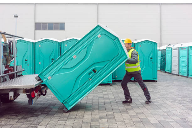 Crew member delivering a portable toilet unit to a construction site